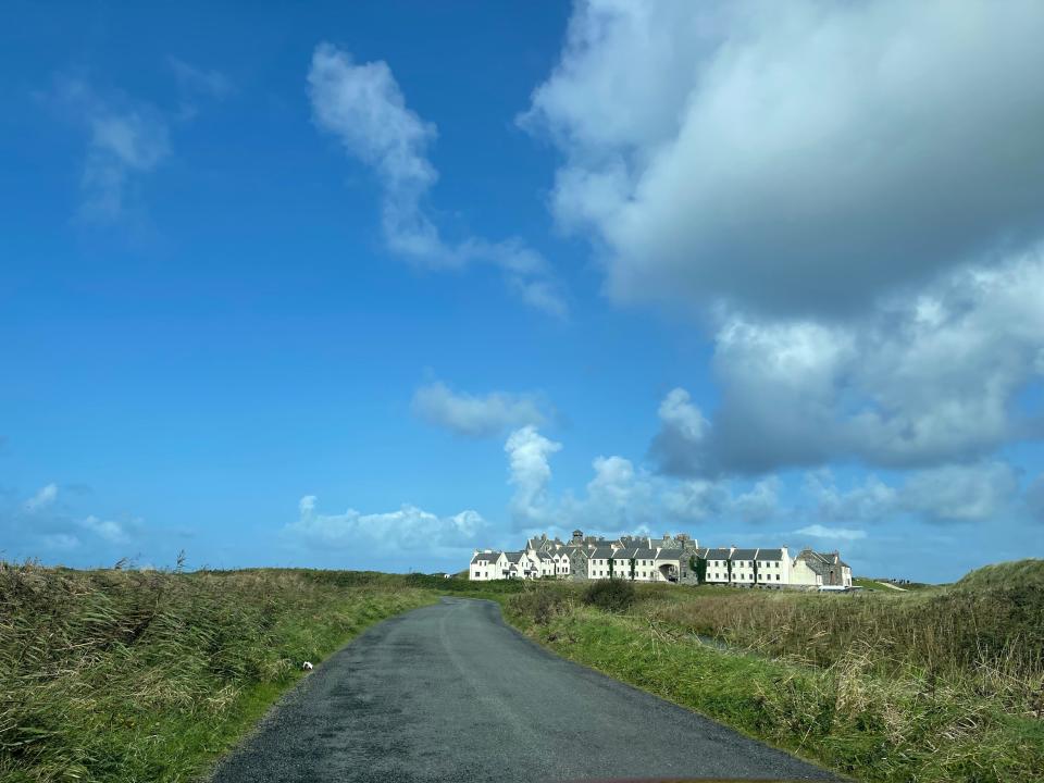 White buildings and Trump International Hotel from a distance. The road is surrounded by grass and bright blue skies