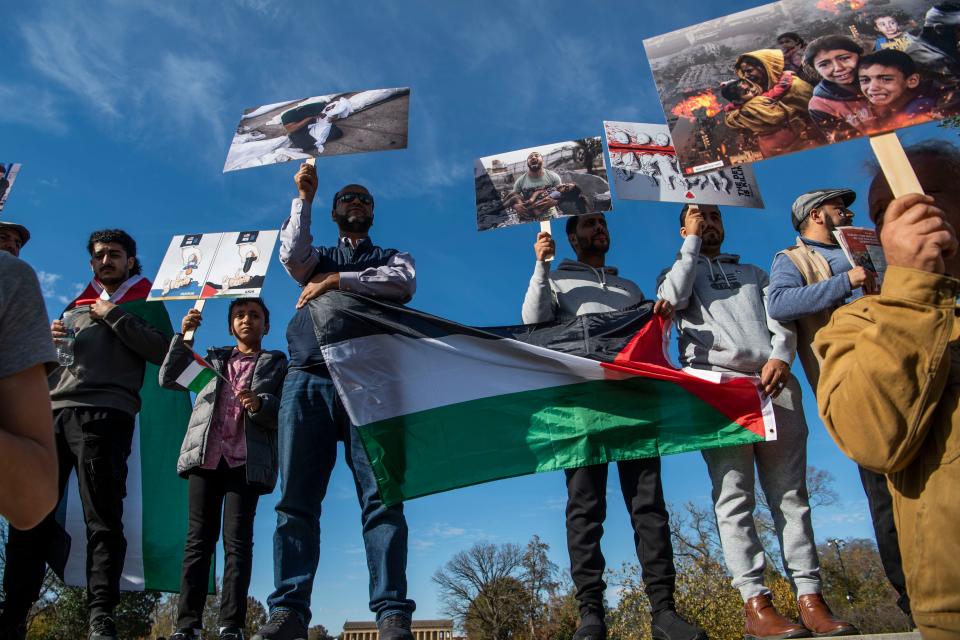 Men stand on the concrete fence in front of Centennial Park's entrance holding up images depicting children of the Israel-Hamas war at a “free Palestine” gathering in Nashville, Tenn., Saturday, Nov. 11, 2023.