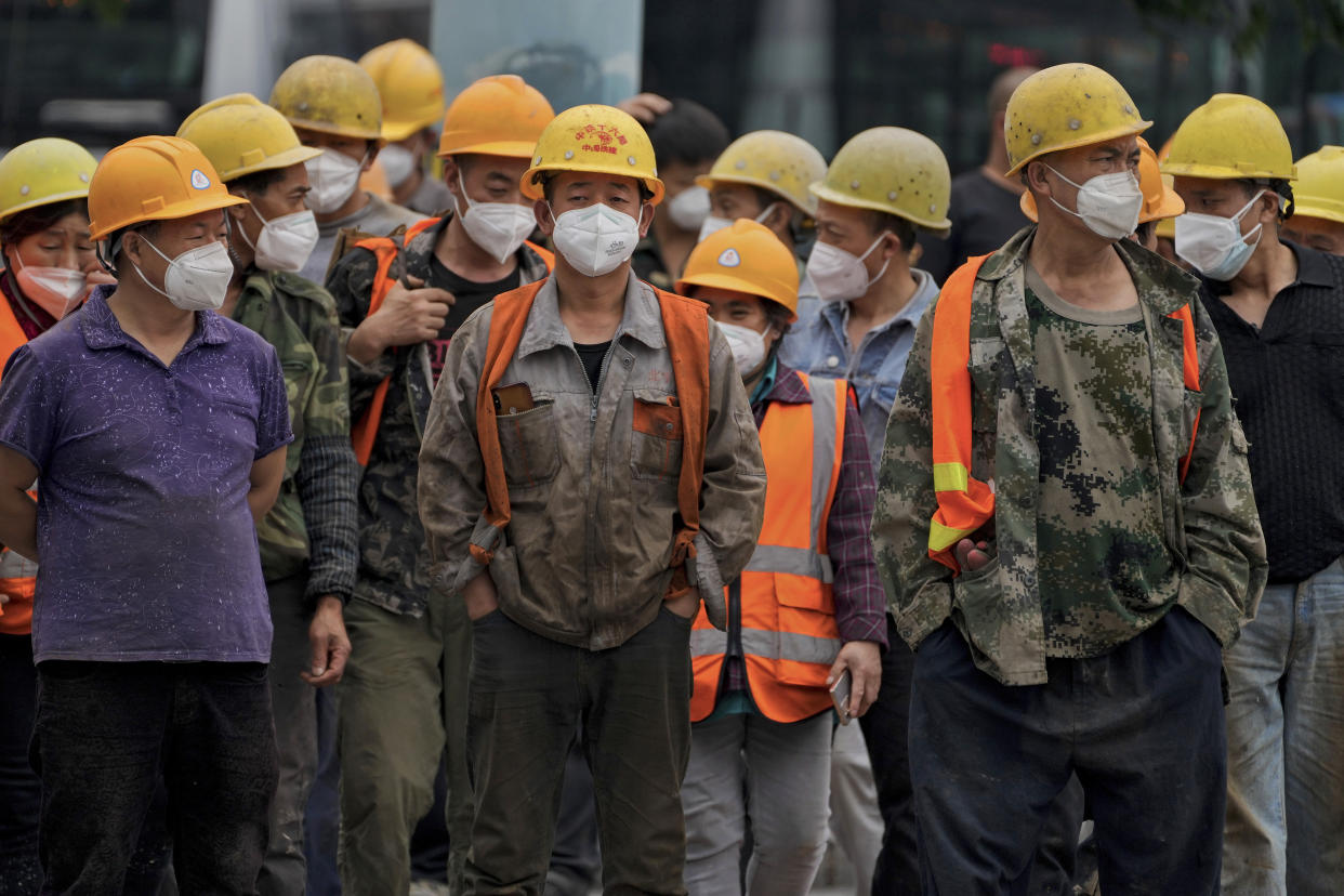 A group of construction workers wearing face masks wait to cross an intersection in Beijing, Monday, June 13, 2022. China's capital has put school online in one of its major districts amid a new COVID-19 outbreak linked to a nightclub, while life has yet to return to normal in Shanghai despite the lifting of a more than two month-long lockdown. (AP Photo/Andy Wong)