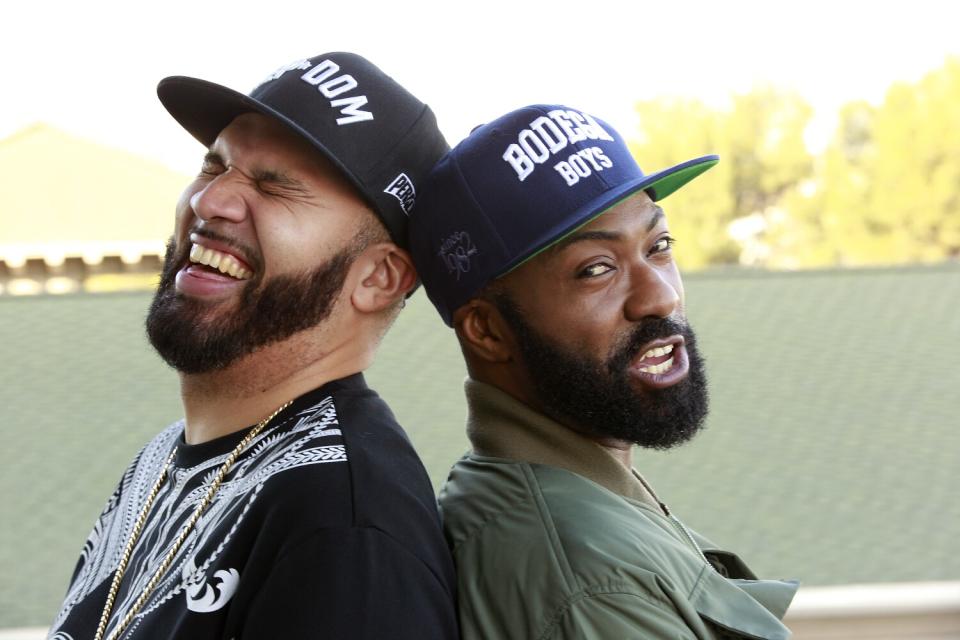 Two men in T-shirts and baseball hats stand back to back.