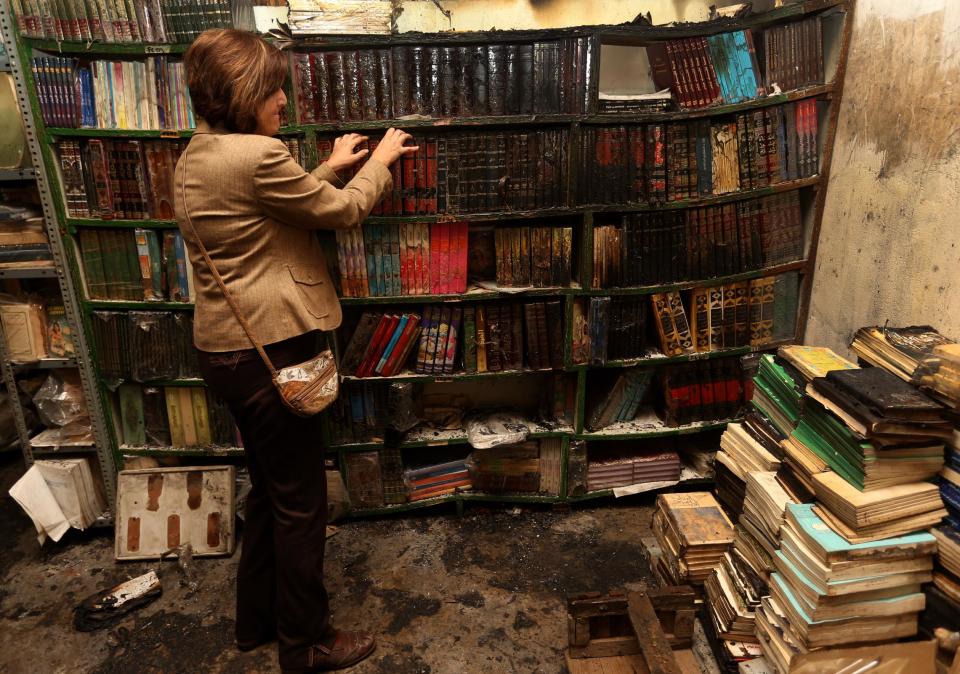 In this picture taken on Sunday January, 5, 2014, a Lebanese woman Najat Bitar, 56, removes burned books, at the Saeh (Tourist) Library which was set on fire by masked men, in the northern city of Tripoli, Lebanon. Books that were burnt in an arson attack targeting a crammed, chaotic and popular library in the northern Lebanese city of Tripoli have become the latest victim of the country's rising sectarian tensions.(AP Photo/Hussein Malla)