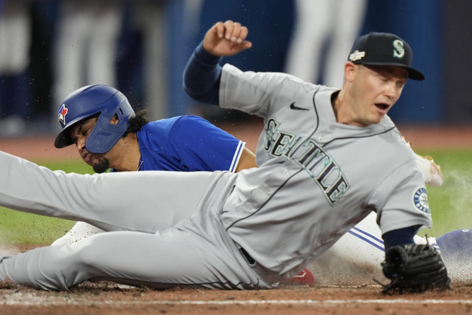 Toronto Blue Jays' Santiago Espinal, left, scores on passed ball as Seattle Mariners relief pitcher Paul Sewald, right, tries to defend during the fifth inning of Game 2 of a baseball AL wild-card playoff series Saturday, Oct. 8, 2022, in Toronto. (Frank Gunn/The Canadian Press via AP)