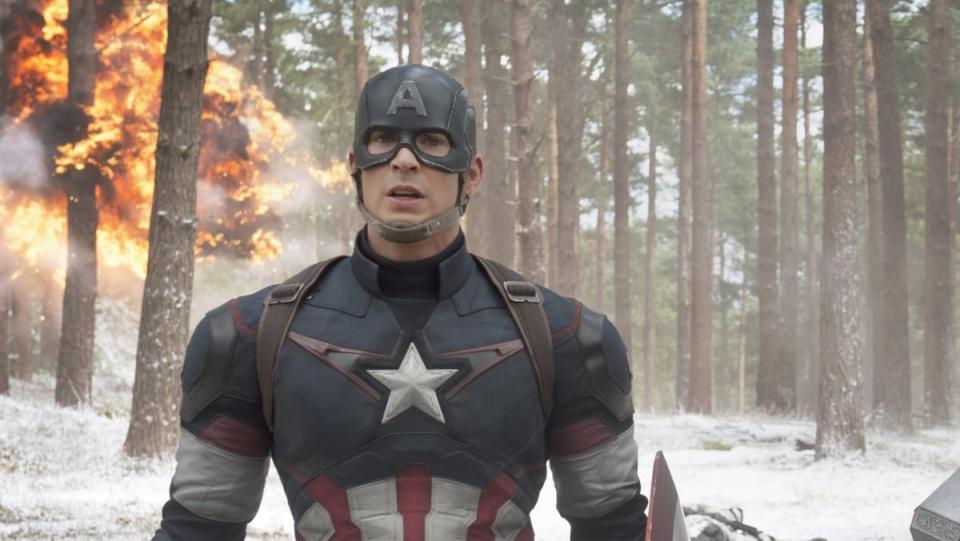 Captain America stands in the wintery woods with fire behind him.