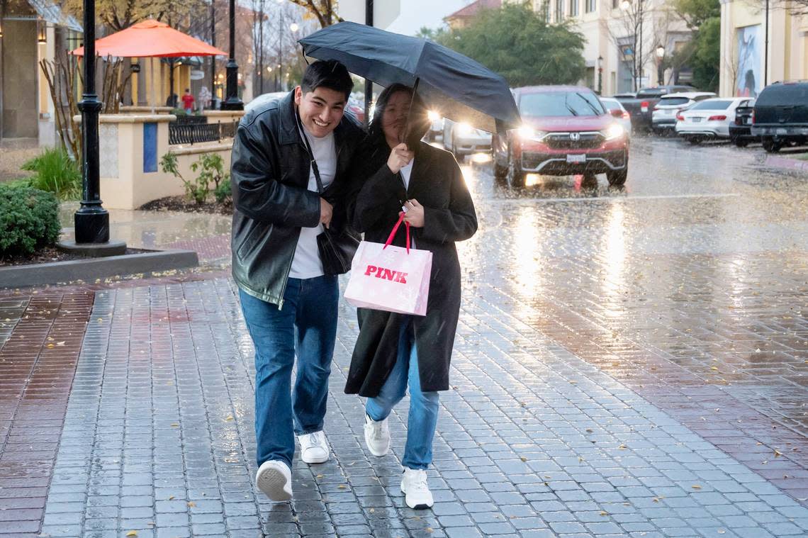 Shoppers share an umbrella while running across the street in the rain on Sunday, Dec. 17, 2023, at the Palladio shopping center in Folsom. Sara Nevis/snevis@sacbee.com