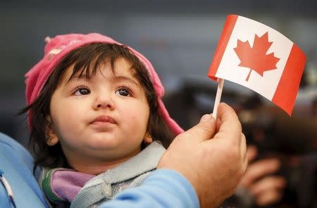 A Syrian refugee looks up as her father holds her and a Canadian flag as they arrive at Pearson Toronto International Airport in Mississauga, Ontario, December 18, 2015. REUTERS/Mark Blinch