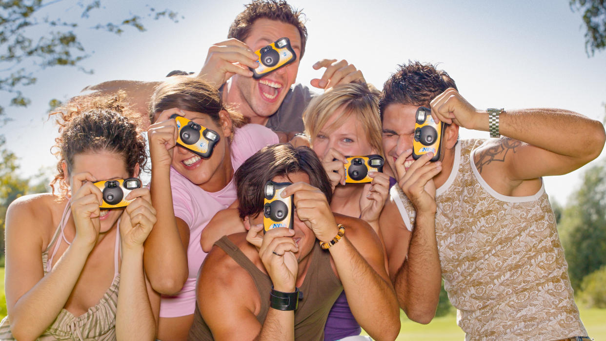  Group of young people aiming their disposable cameras towards the viewer 