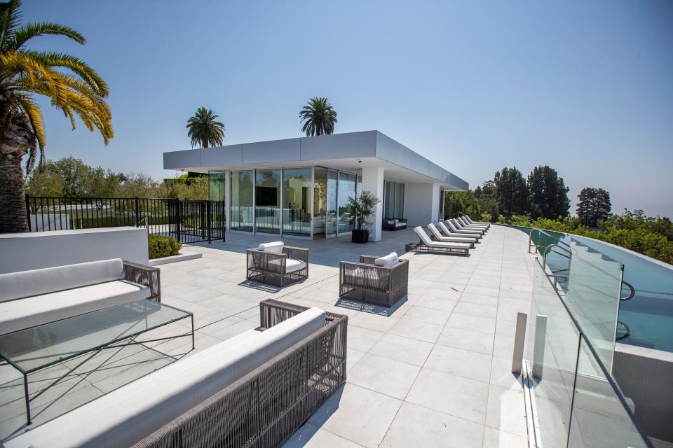 a white guest house at mansion The One Bel Air with palm trees and white chairs nearby