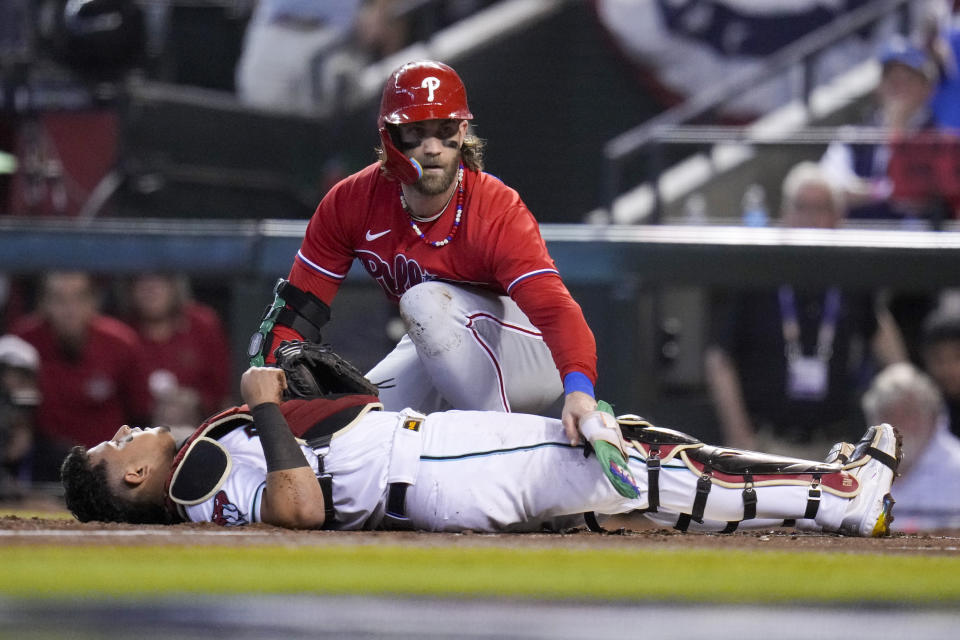 Philadelphia Phillies' Bryce Harper checks on Arizona Diamondbacks catcher Gabriel Moreno after a collision during the first inning in Game 5 of the baseball NL Championship Series in Phoenix, Saturday, Oct. 21, 2023. (AP Photo/Ross D. Franklin)