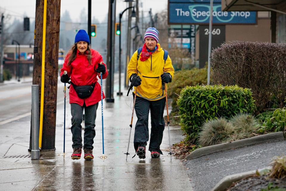Barb Hazen, left, and Mari Baldwin use trekking poles and ice spikes to navigate the ice along Willamette Street on their way to a volunteer shift at the Egan Warming Center at the Lane Events Center Friday morning.