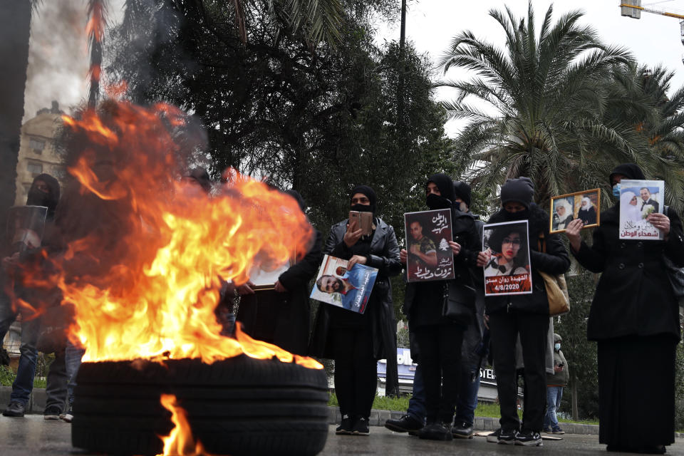 Relatives of victims of the Aug. 4, 2020 Beirut port explosion hold portraits of their loved one who killed during the explosion, as they burn tires to block a road during a sit-in outside the Justice Palace, in Beirut, Lebanon, Friday, Feb. 19, 2021. The prosecutor investigating last year's massive blast in Beirut was formally notified Friday that he would no longer lead an enquiry into last year's deadly port explosion, state-run Lebanon's National News Agency reported. (AP Photo/Bilal Hussein)