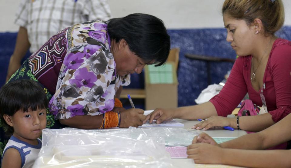 A Guna indigenous woman accompanied by her son signs a paper after casting her vote at a polling station in Loma Cova on the outskirts of Panama City, Sunday, May 4, 2014. Panamanians are choosing a new president in a three-way dogfight marked more by ugly personality clashes between the candidates, than any deep disagreements over the way forward for Latin America's standout economy. (AP Photo/Tito Herrera)