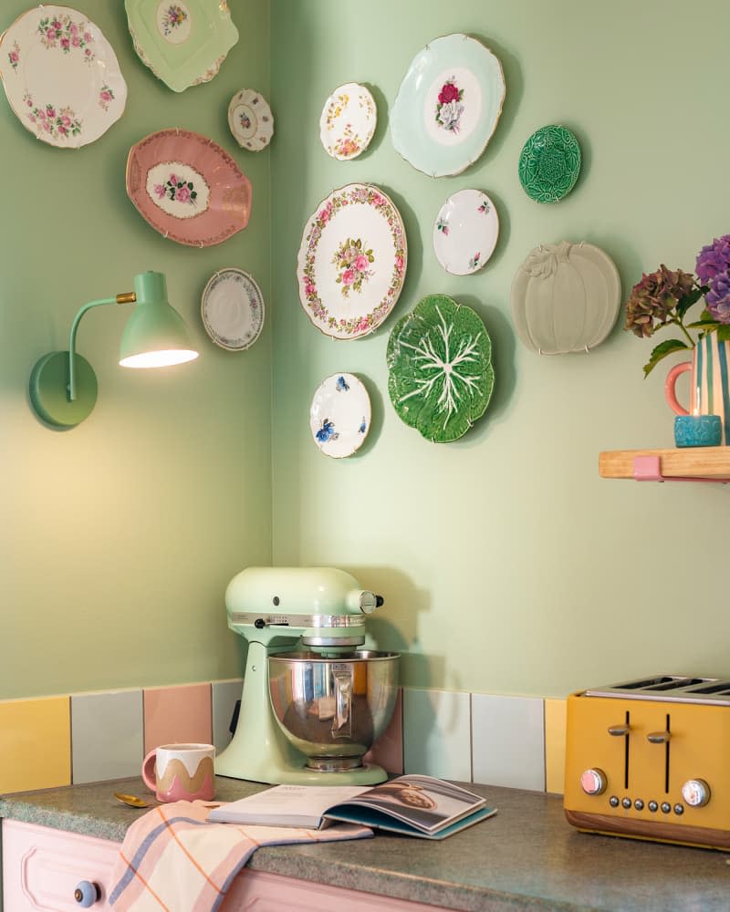 Decorative plates hang on pastel green wall above pastel mixer and toaster in kitchen.