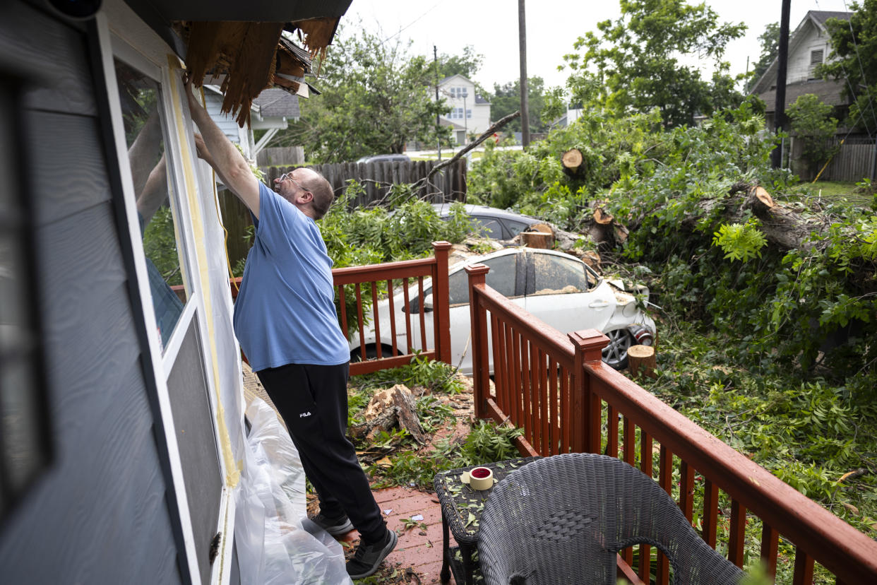 Dan Beagen tapes of a broken window after a pecan tree fell on cars and his home during a wind storm the night before in Houston, May 17, 2024. (Annie Mulligan/The New York Times)