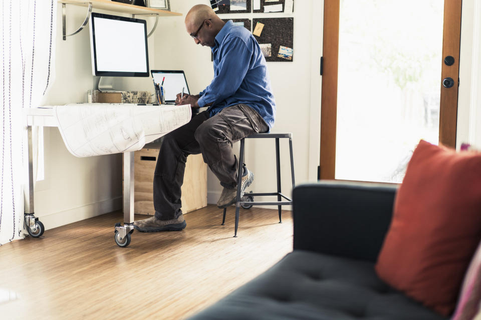 Architect looking a blueprint at desk in home office while sitting on stool