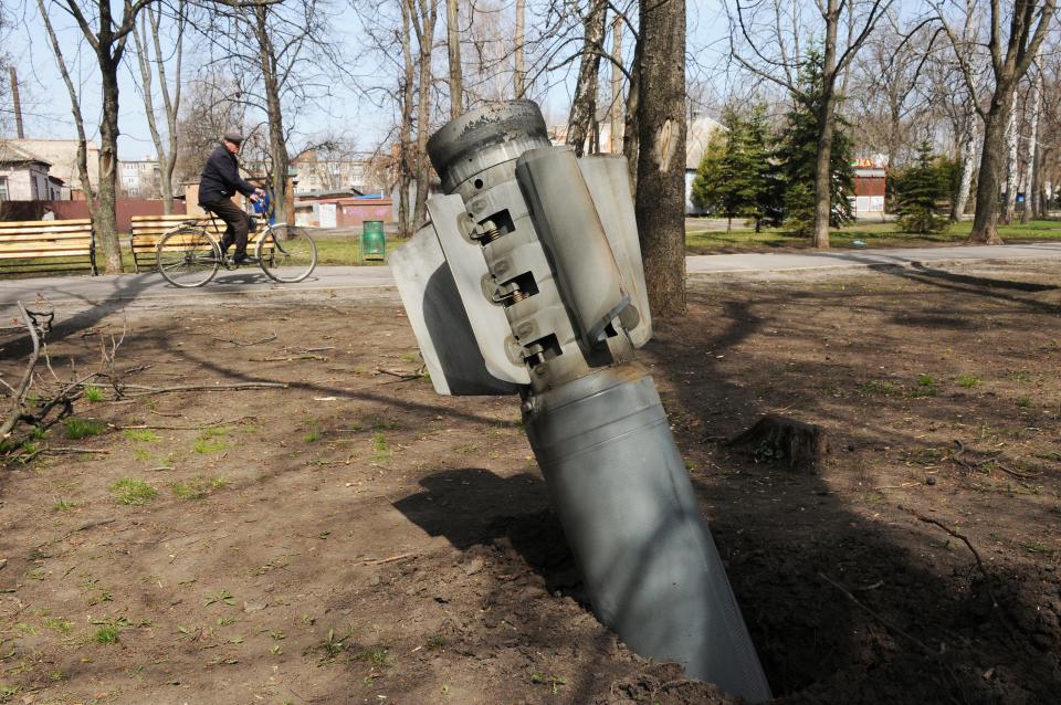 A man rides a bicycle as a tail of a missile sticks out in the city of Chuhuiv, Kharkiv region, Ukraine, Friday, April 8, 2022. AP Photo/Andrew Marienko