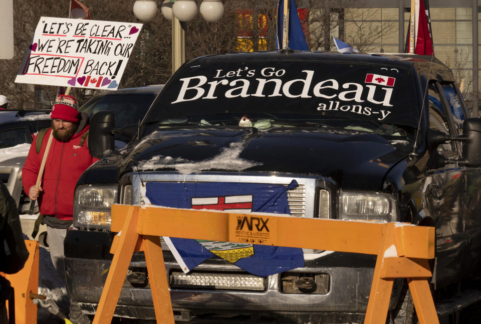 A protester walks past a truck parked in the street in the downtown core during a demonstration against COVID-19 restrictions, Saturday, Feb. 5, 2022, in Ottawa, Ontario. (Adrian Wyld/The Canadian Press via AP)