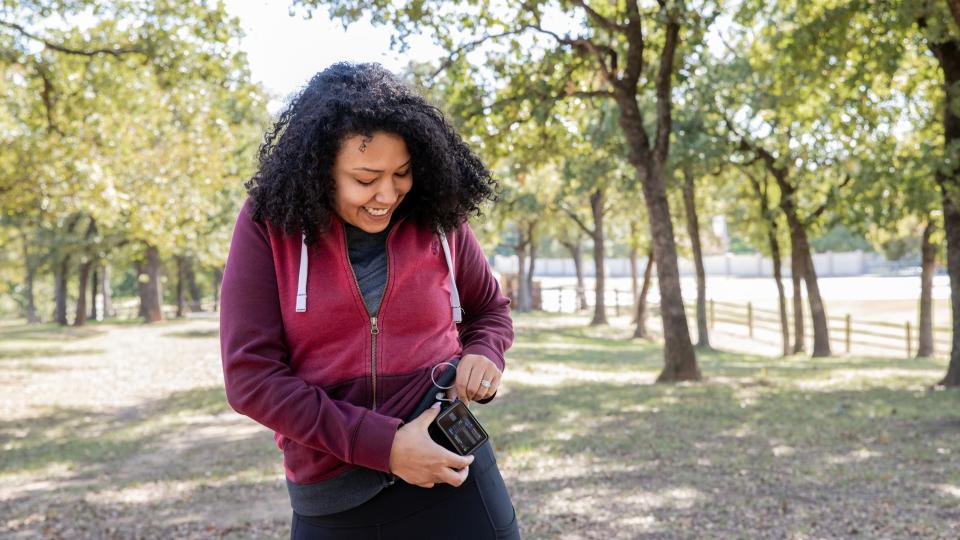 Young woman checks insulin pump and blood sugar monitor while hiking outdoors