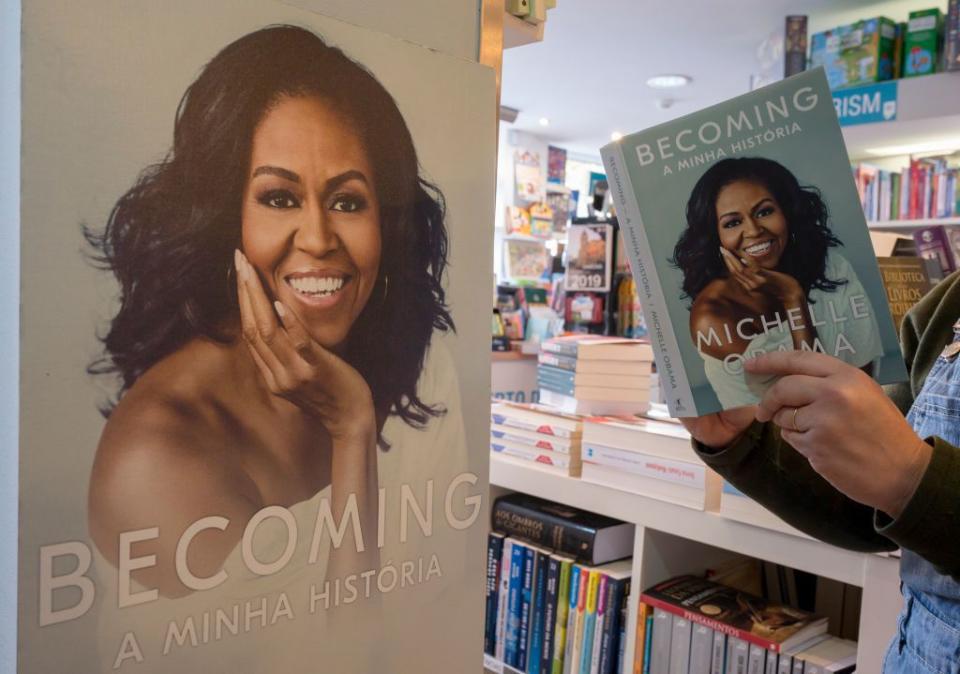 a man holds open a copy of the michelle obama book becoming, in a bookstore, while standing next to a large cardboard image of the book cover