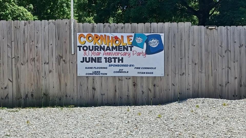 A sign for the Cornhole Tournament is seen on a fence.