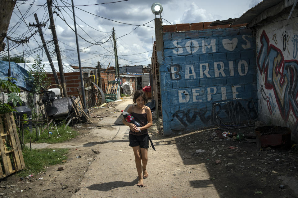 A girl carries a soft drink bottle through the Puerta 8 suburb north of Buenos Aires, Argentina, where police say contaminated cocaine may have been sold, Friday, Feb. 4, 2022. A batch of cocaine has killed at least 23 people and hospitalized many more in Argentina, according to police. (AP Photo/Rodrigo Abd)