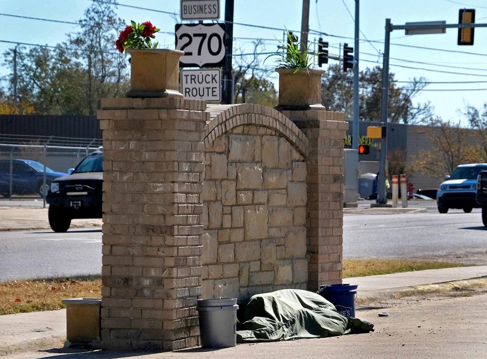 A person lies under a blanket Nov. 6 up against a sign in front of Homeless Resource Center in Shawnee.
