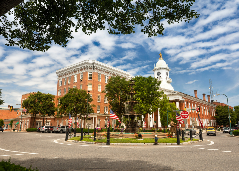 A roundabout in the center with a red-bricked building with a clock tower standing tall in the background.