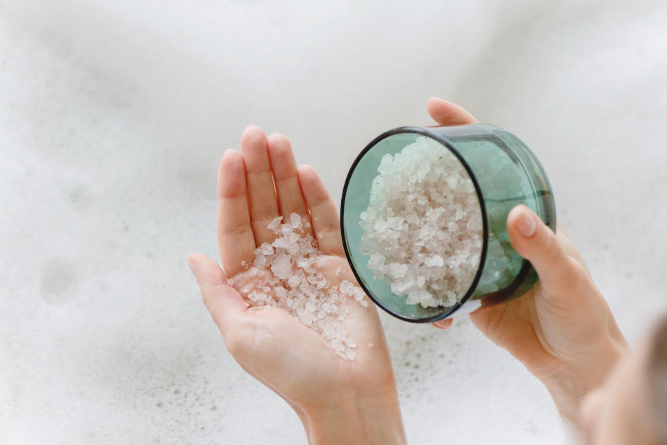 Closeup of sea bath salt in woman hands against the background of foam bath.