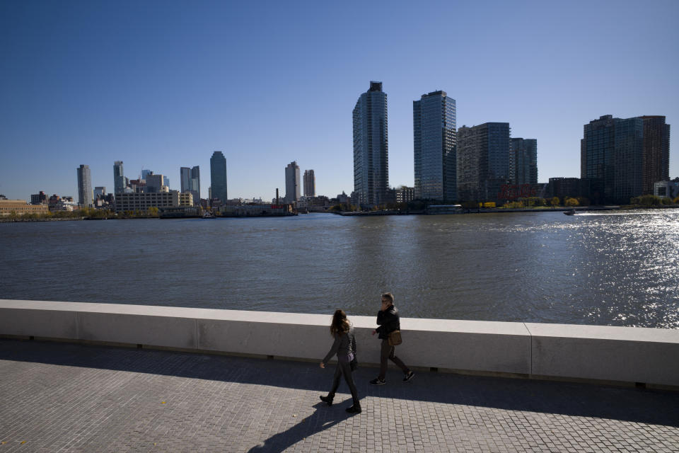 FILE- In this Nov. 7, 2018, file photo a couple walks along Four Freedoms State Park on Roosevelt Island in the Queens borough of New York. Beyond is the Long Island City skyline. According to experts analyzing the e-commerce giant's sudden cancellation of plans to build a massive headquarters in New York City, Amazon's decision to walk away could scare off other tech companies considering moving to or expanding in the city. (AP Photo/Mark Lennihan, File)