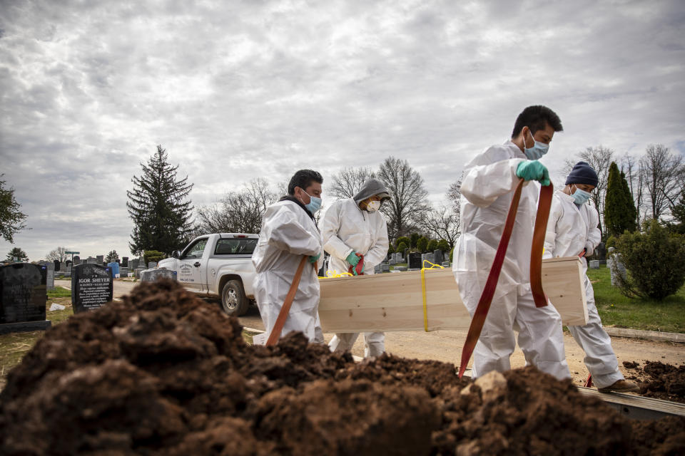 Gravediggers carry the casket of someone presumed to have died from coronavirus as they are buried without any family present at Mount Richmond Cemetery in the Staten Island borough of New York, Tuesday, April 7, 2020. In a marathon of grief at this small Jewish cemetery mounds of dirt are piling up as graves are opened, vans are constantly arriving with bodies aboard and a line of white signs is being pressed into the ground marking plots soon to be occupied. Families are being kept away from their loved one's gravesite at the cemetery, which caters to those with little or nothing. (AP Photo/David Goldman)