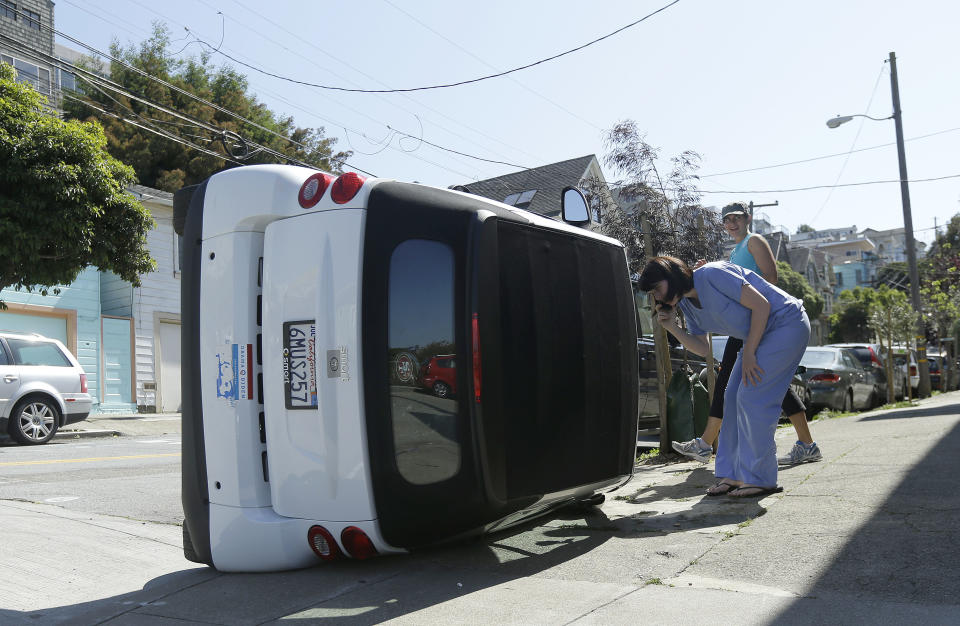 Shelley Gallivan, foreground right, looks into a tipped over Smart car which belongs to her friend on the corner of Prospect and Oso streets in San Francisco, Monday, April 7, 2014. Police in San Francisco are investigating why four Smart cars were flipped over during an apparent early morning vandalism spree. Officer Gordon Shyy, a police spokesman, says the first car was found flipped on its roof and a second was spotted on its side around 1 a.m. Monday in the Bernal Heights neighborhood. (AP Photo/Jeff Chiu)