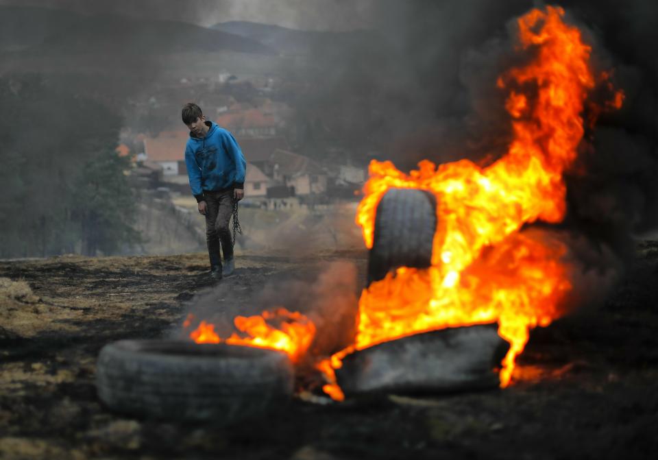 In this photo taken on Sunday, March 10, 2019, a boy walks holding a metal chain, during a ritual marking the upcoming Clean Monday, the beginning of the Great Lent, 40 days ahead of Orthodox Easter, on the hills surrounding the village of Poplaca, in central Romania's Transylvania region. Romanian villagers burn piles of used tires then spin them in the Transylvanian hills in a ritual they believe will ward off evil spirits as they begin a period of 40 days of abstention, when Orthodox Christians cut out meat, fish, eggs, and dairy. (AP Photo/Vadim Ghirda)