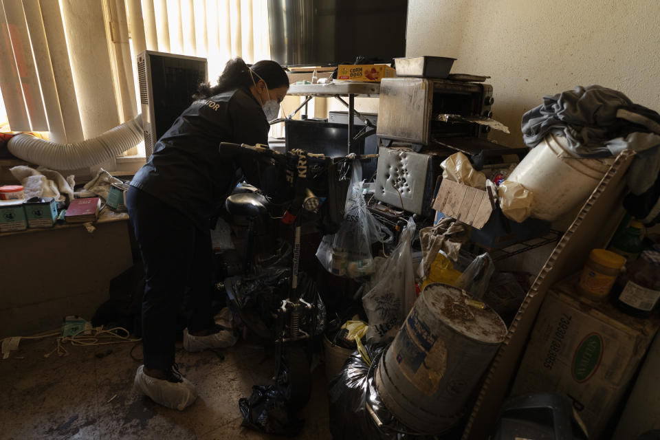 Arusyak Martirosyan, an investigator with the Los Angeles County Public Administrator's office, searches through a cluttered micro-apartment in Los Angeles, Wednesday, Dec. 13, 2023, for clues that might lead to finding family members or relatives of a tenant who was found dead in his bed. (AP Photo/Jae C. Hong)