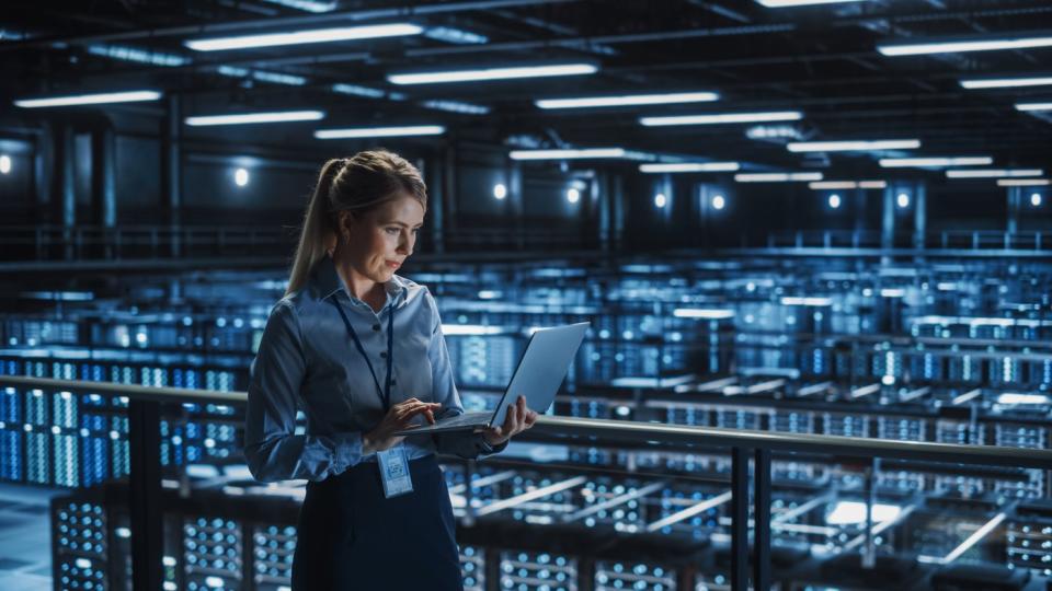 An IT professional checks a laptop computer in a server room.