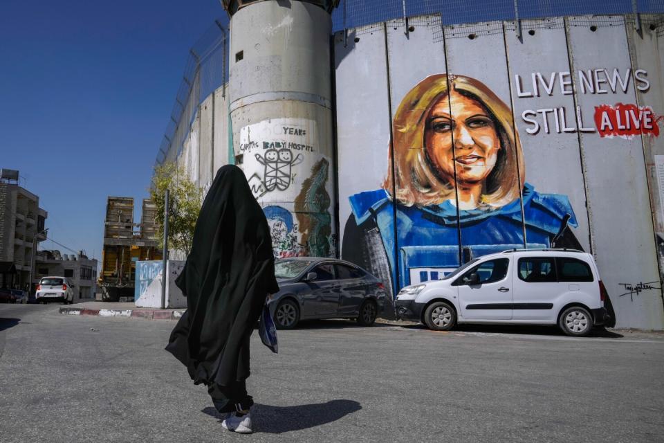 A person in a veil walks past a mural of slain journalist Shireen Abu Akleh.