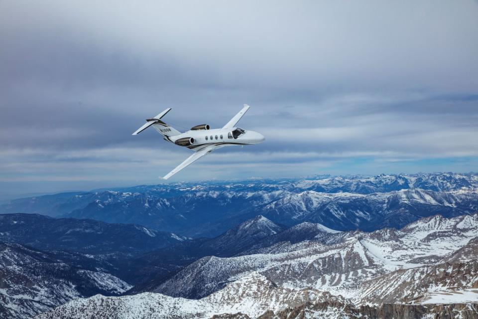 Cessna Citation M2 flying over snowy mountains.