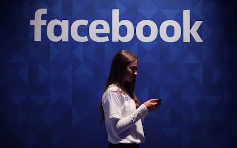 A woman using her phone under a Facebook logo - Credit: Niall Carson/ PA