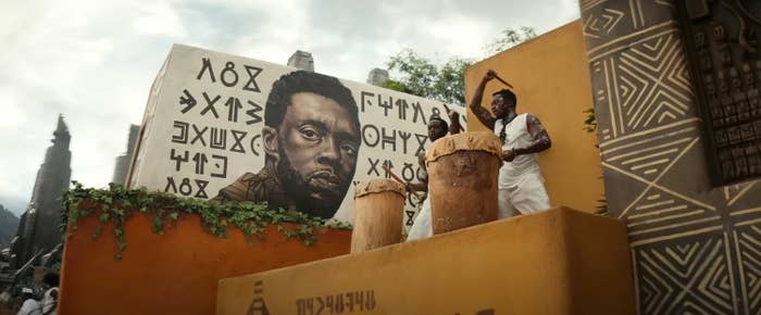 An mural of T'Challa alongside men beating drums on a platform