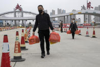 In this Thursday, April 2, 2020, photo, a man and woman carry eggs as they cross the expressway gate at the border into Wuhan city in central China's Hubei province. Millions of Chinese workers are streaming back to factories, shops and offices but many still face anti-coronavirus controls that add to their financial losses and aggravation. In Wuhan police require a health check and documents from employers for returning workers. (AP Photo/Ng Han Guan)