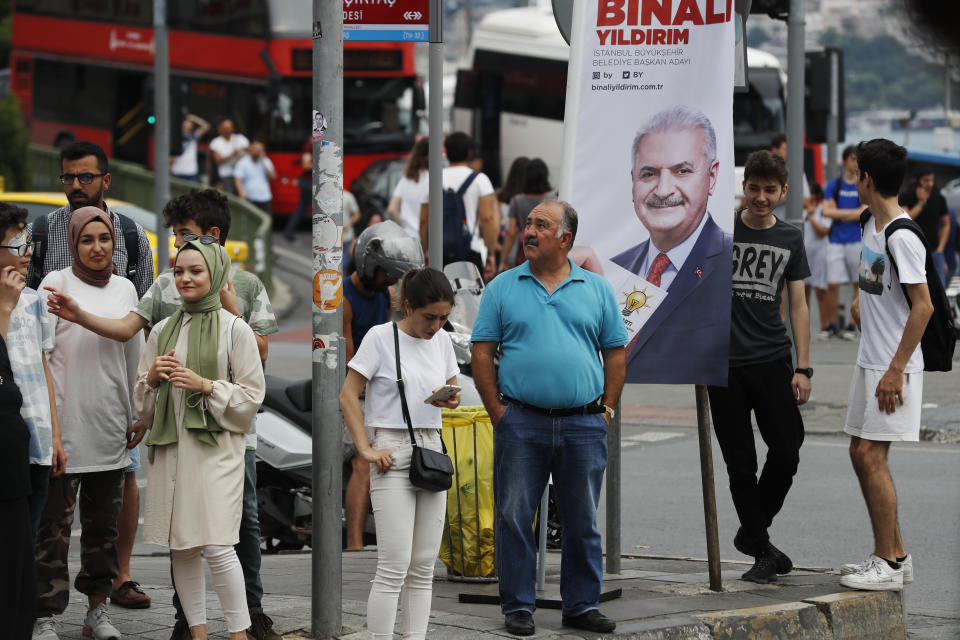 In this Wednesday, June 19, 2019 photo, people walk past a poster of Istanbul's mayoral candidate Binali Yildirim, of Turkey's ruling Justice and Development Party, or AKP, in Istanbul, ahead of the June 23 re-run of Istanbul elections. Millions of voters in Istanbul go back to the polls for a controversial mayoral election re-run Sunday, as President Recep Tayyip Erdogan's party tries to wrest back control of Turkey's largest city. (AP Photo/Lefteris Pitarakis)