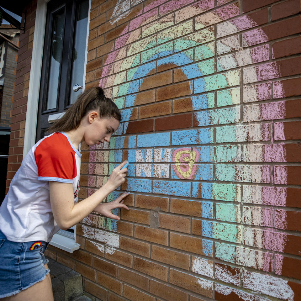 A teenager draws a rainbow and an NHS logo on the wall of her house in Liverpool in support of the NHS as the UK continues in lockdown to help curb the spread of the coronavirus.