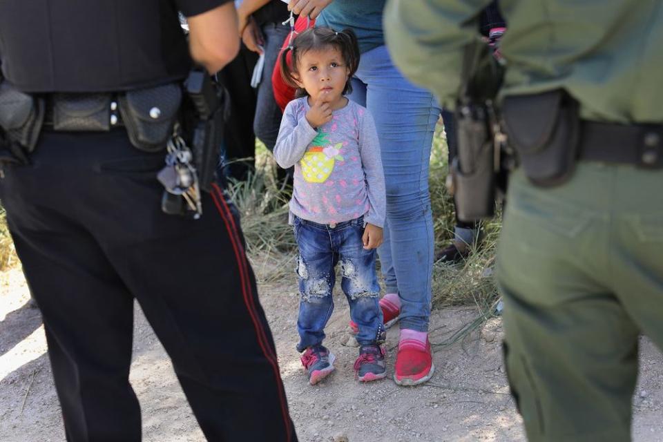 A Mission Police Dept. officer (L), and a U.S. Border Patrol agent watches over a group of Central American asylum seekers before taking them into custody near McAllen, Texas