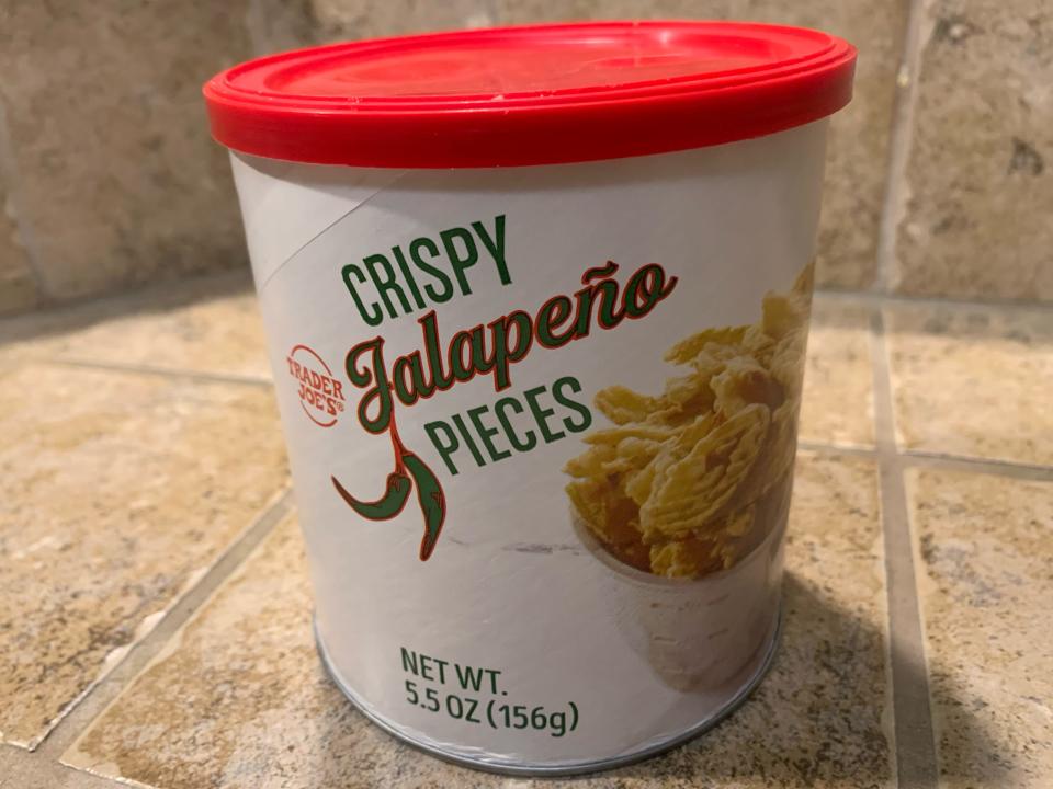 Trader joe's crispy jalepeno pieces in its original white and red container against beige tile