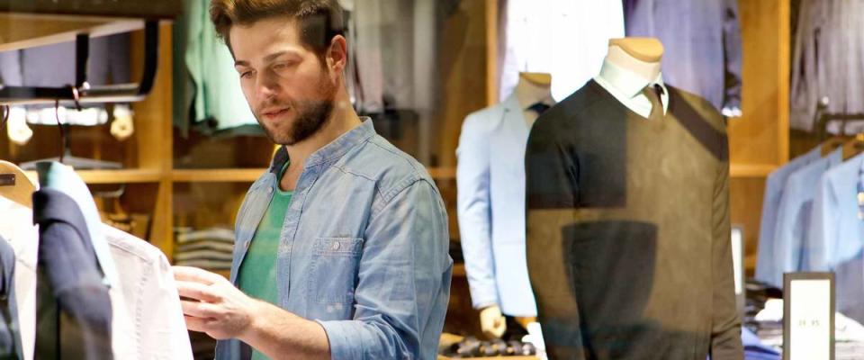 Portrait of a young man looking at clothes to buy at shop