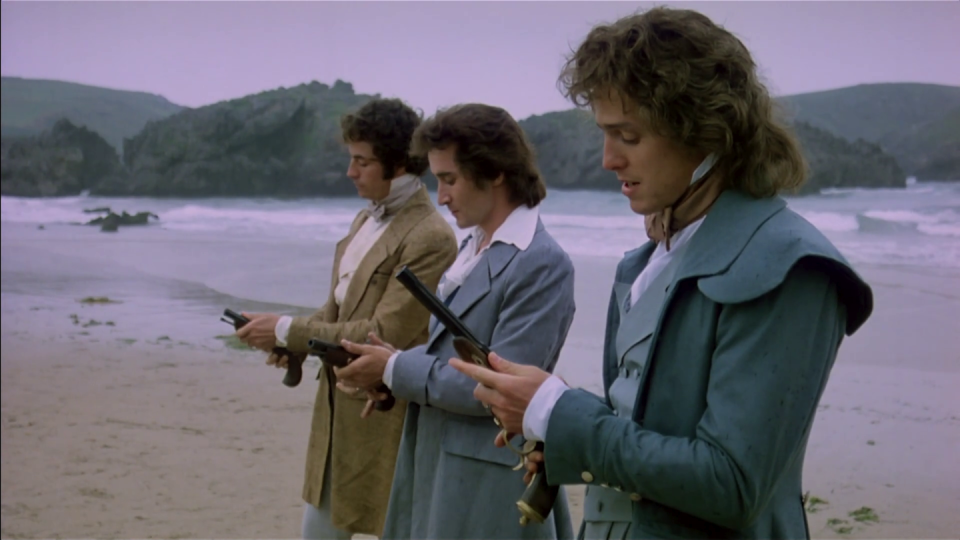 Tres hombres vestidos de época cargan sus pistolas en una playa.