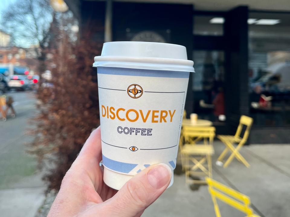 hand holding up a to-go cup of discovery coffee in front of discovery coffee cafe