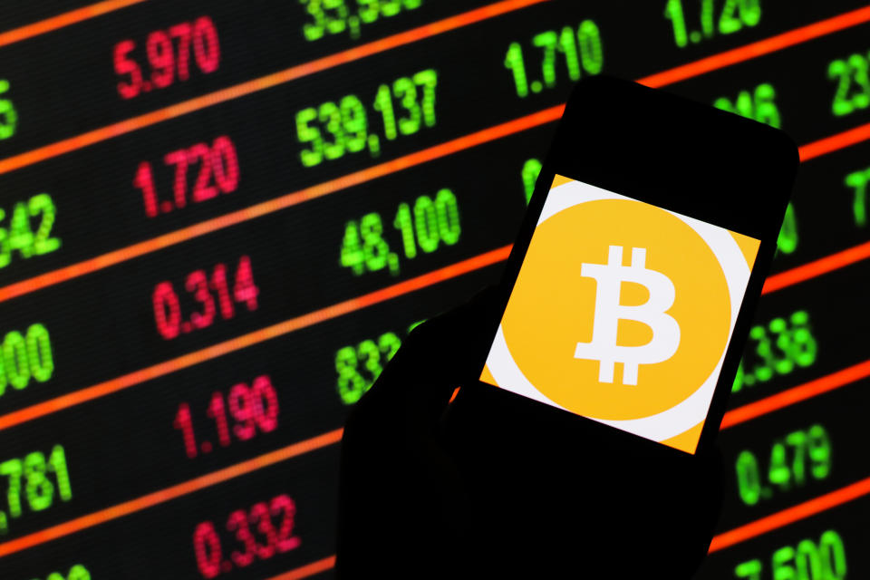 POLAND - 2020/03/13: In this photo illustration a Bitcoin cryptocurrency logo seen displayed on a smartphone. Stock market prices in the background as stock markets tumble all over the world. (Photo by Filip Radwanski/SOPA Images/LightRocket via Getty Images)