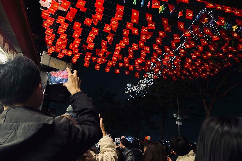 A man takes photographs of a drone light show to celebrate the Lunar New Year while standing on a road lined with the Vietnamese national flags in Hanoi, Vietnam, Friday, Feb. 9, 2024.