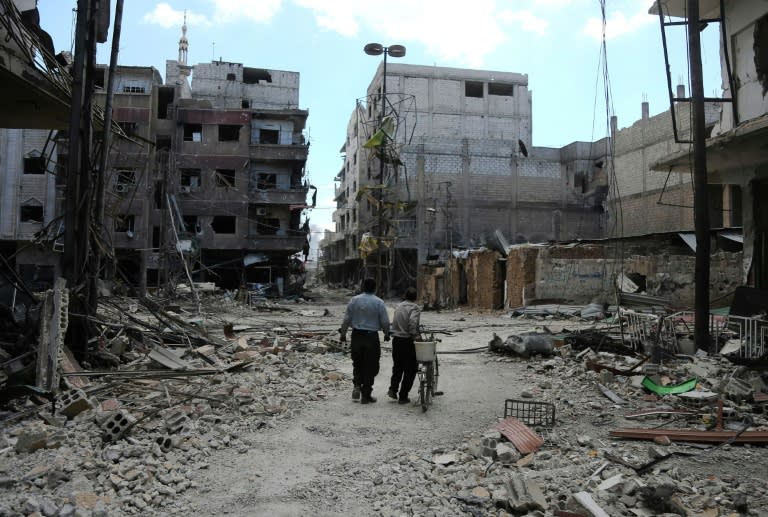 Syrians walk along a destroyed street in the rebel-held town of Arbin in Eastern Ghouta on March 16, 2018, as Syrian pro-government troops advance though the enclave outside Damascus