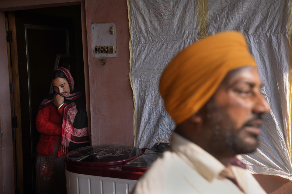 Amarjeet Singh's wife stands outside kitchen as her husband, right, talks in his family home in Kaler Ghuman village, some 40 kilometers (24 miles) from Amritsar, in Indian state of Punjab, Tuesday, Feb. 15, 2022. "Where did those 700-750 farmers go then? The Modi government is responsible for their deaths," said Singh, while talking to The Associated Press. India's Punjab state will cast ballots on Sunday that will reflect whether Indian Prime Minister Narendra Modi's ruling Bharatiya Janata Party has been able to neutralize the resentment of Sikh farmers by repealing the contentious farm laws that led to year-long protests. (AP Photo/Manish Swarup)