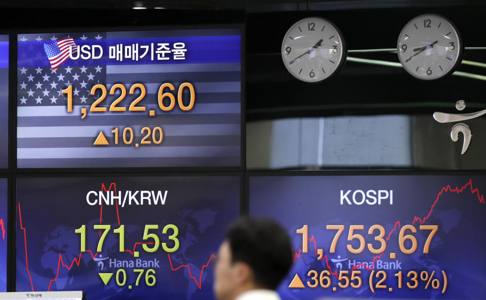 A currency trader walks by the screens showing the Korea Composite Stock Price Index (KOSPI), right, and the foreign exchange rate between U.S. dollar and South Korean won, left top, at the foreign exchange dealing room in Seoul, South Korea, Tuesday, March 31, 2020. Asian shares surged Tuesday after a rally in U.S. stocks, mostly spurred by health care companies' announcements of developments that could aid in the coronavirus outbreak. (AP Photo/Lee Jin-man)
